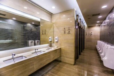 Modern public men's restroom with multiple urinals, sinks, and stalls in a clean, well-lit setting.