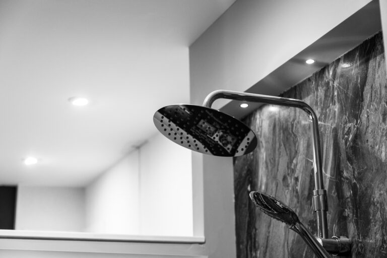 A black-and-white close-up of a sleek showerhead mounted on a marble wall.